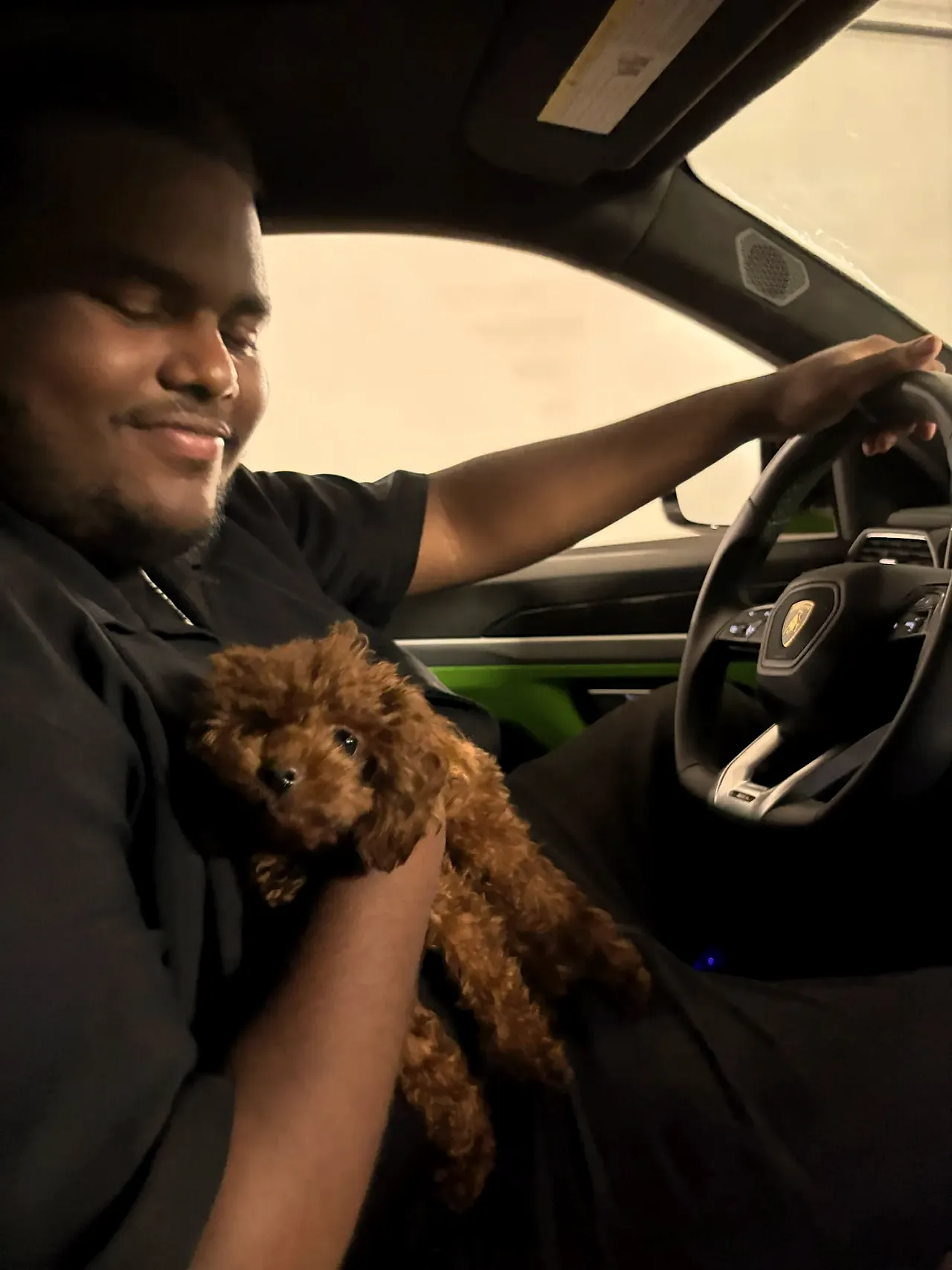 Negus in the driver’s seat of a Lamborghini, holding a puppy.